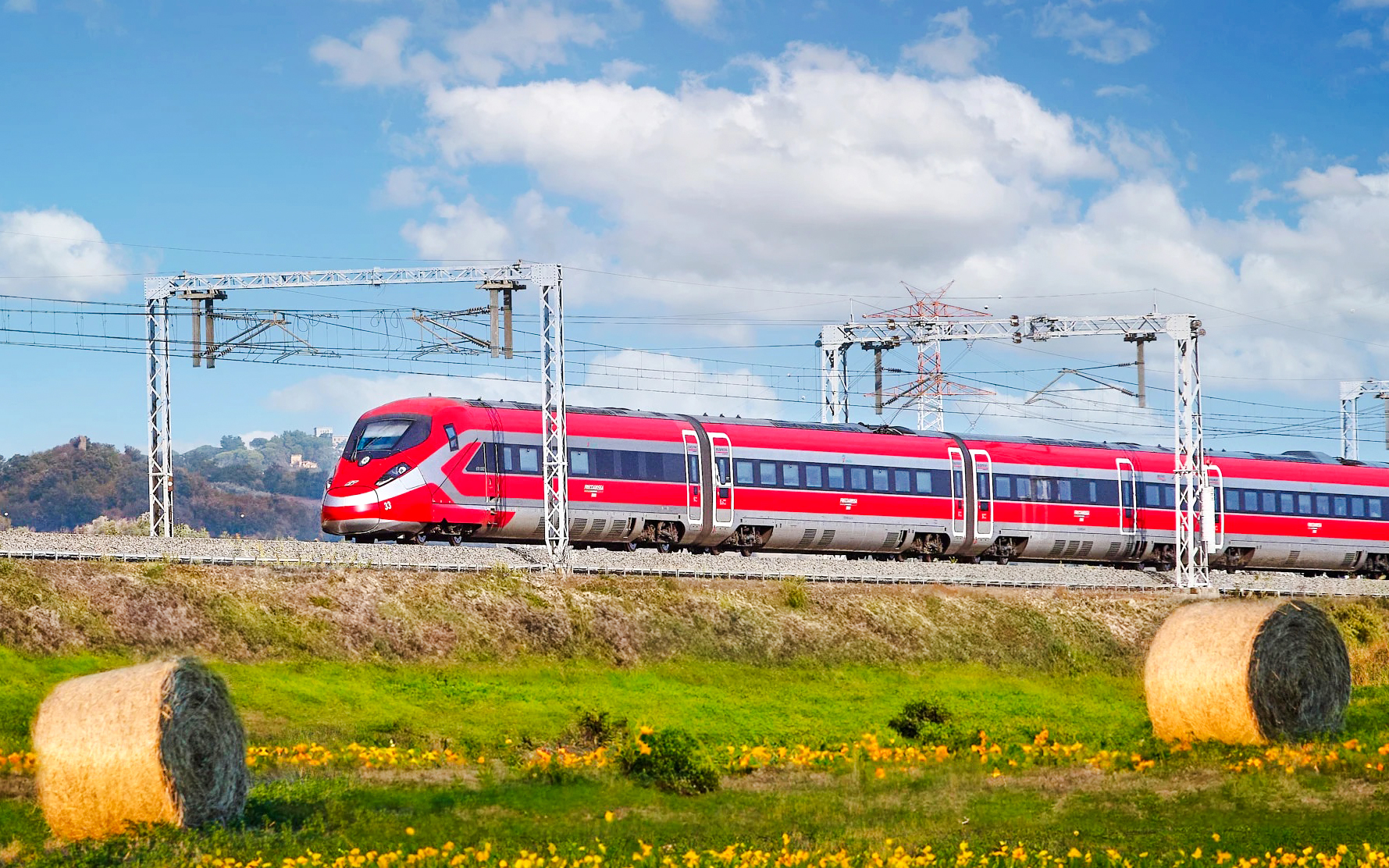Trenitalia Frecciarossa train traveling through scenic countryside with hay bales.