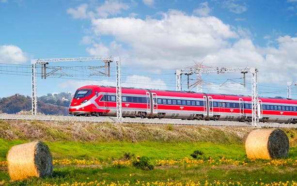 Trenitalia Frecciarossa train traveling through scenic countryside with hay bales.