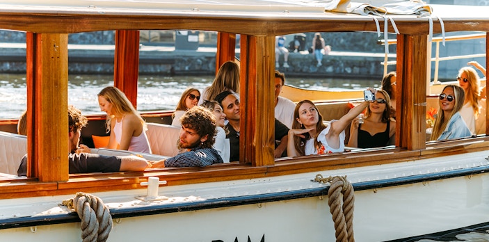 Tourists on a saloon boat cruise in Amsterdam, taking photos and enjoying the view.