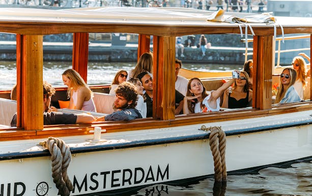 Tourists on a saloon boat cruise in Amsterdam, taking photos and enjoying the view.