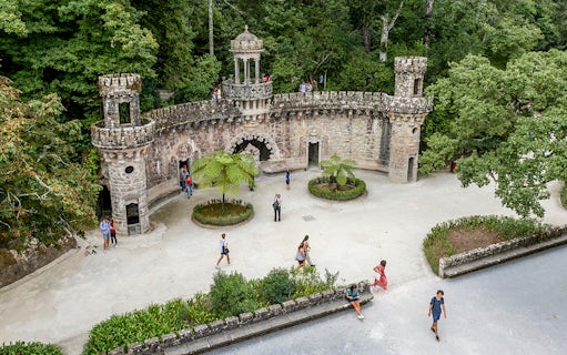 Guided tour group exploring gardens at Quinta da Regaleira, Sintra, near stone structure.
