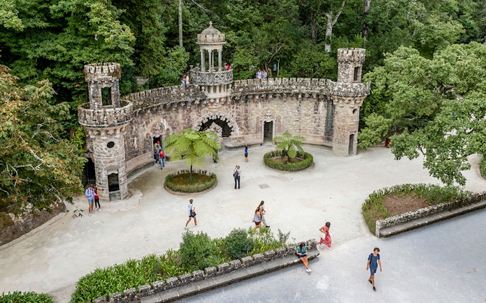 Guided tour group exploring gardens at Quinta da Regaleira, Sintra, near stone structure.