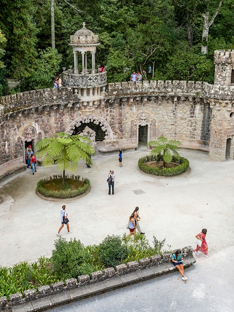 Guided tour group exploring gardens at Quinta da Regaleira, Sintra, near stone structure.