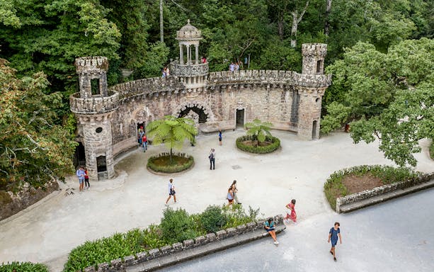 Guided tour group exploring gardens at Quinta da Regaleira, Sintra, near stone structure.