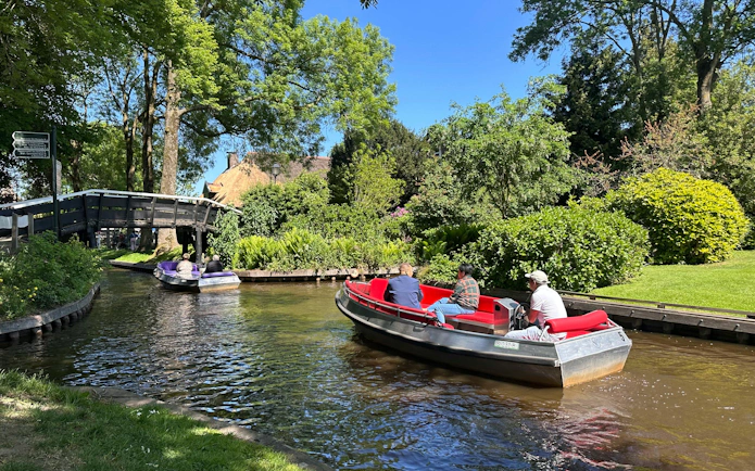 Boat navigating canal under bridge in Giethoorn, surrounded by lush greenery.