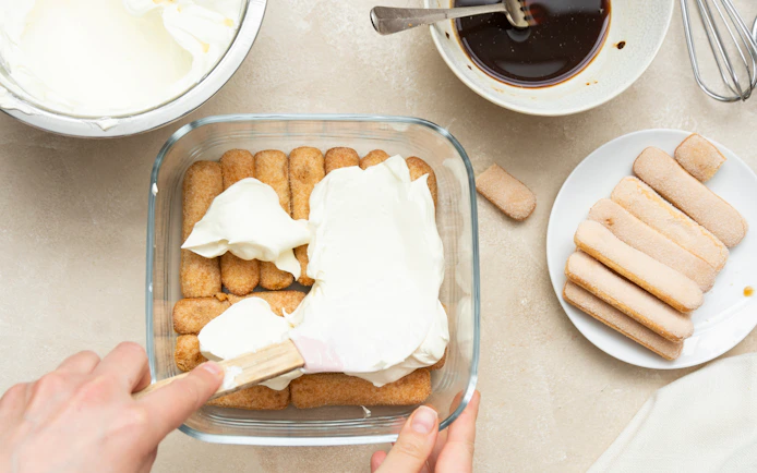 Spreading mascarpone over ladyfingers for tiramisu preparation.