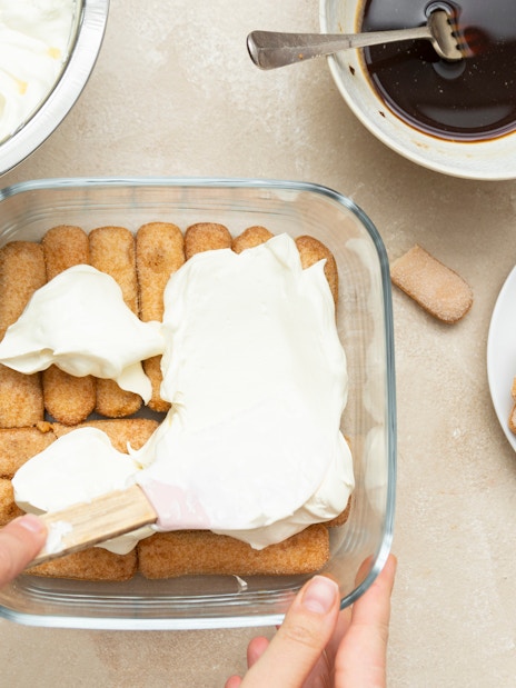 Spreading mascarpone over ladyfingers for tiramisu preparation.