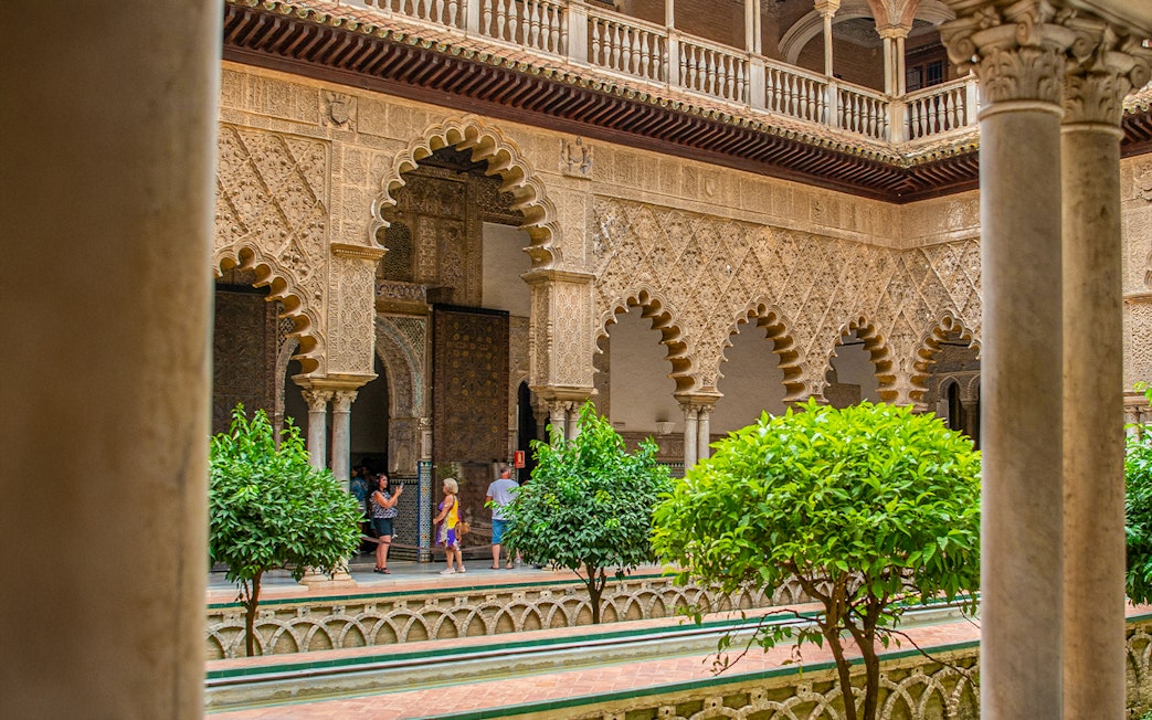 Tour group exploring Moorish arches in Alcazar of Seville courtyard.