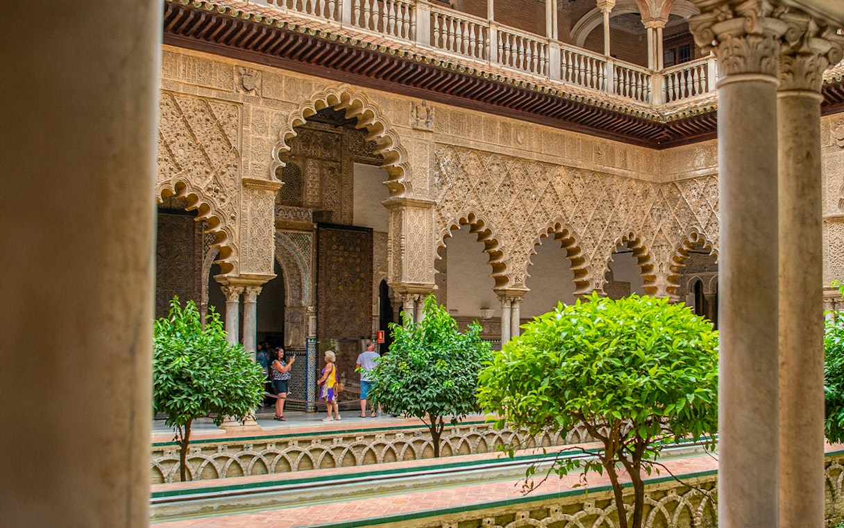 Tour group exploring Moorish arches in Alcazar of Seville courtyard.