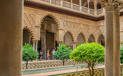 Tour group exploring Moorish arches in Alcazar of Seville courtyard.