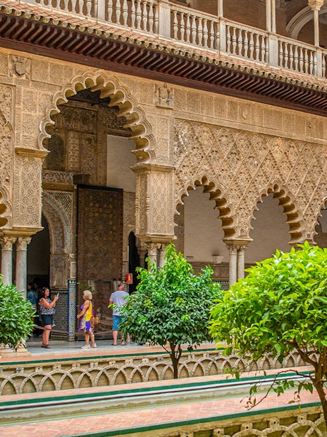 Tour group exploring Moorish arches in Alcazar of Seville courtyard.