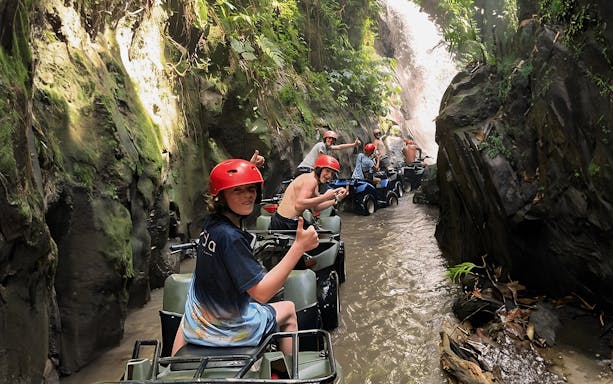 ATV riders in Ubud navigating a lush, narrow tunnel with a waterfall.