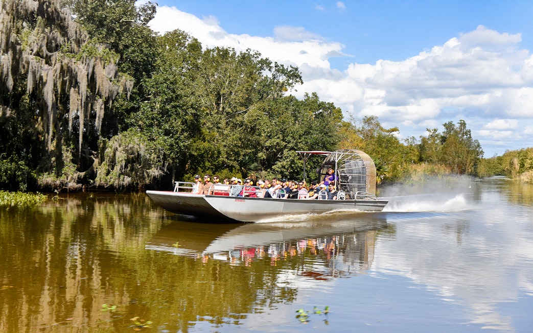 Airboat with tourists on a swamp tour in New Orleans, surrounded by trees and water.