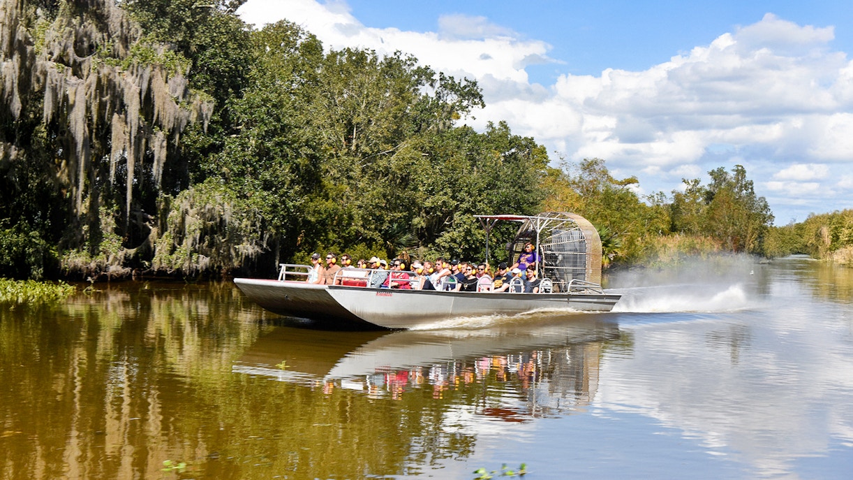 Airboat with tourists on a swamp tour in New Orleans, surrounded by trees and water.