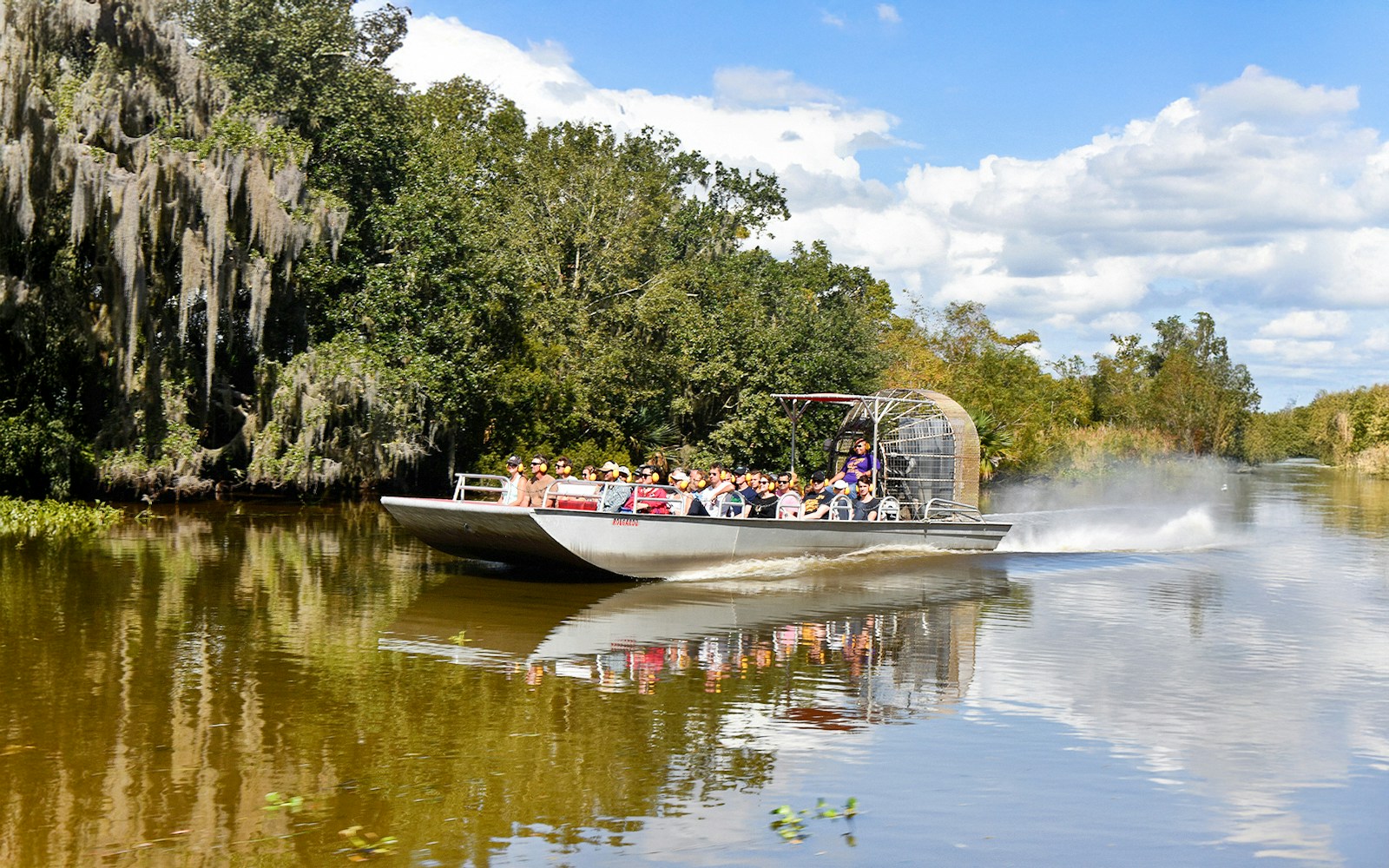 Airboat with tourists on a swamp tour in New Orleans, surrounded by trees and water.