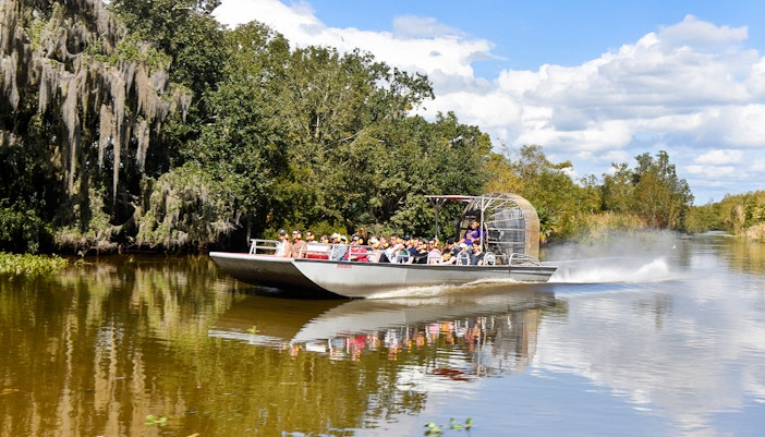 Airboat with tourists on a swamp tour in New Orleans, surrounded by trees and water.