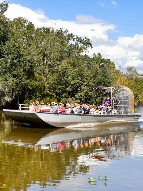 Airboat with tourists on a swamp tour in New Orleans, surrounded by trees and water.
