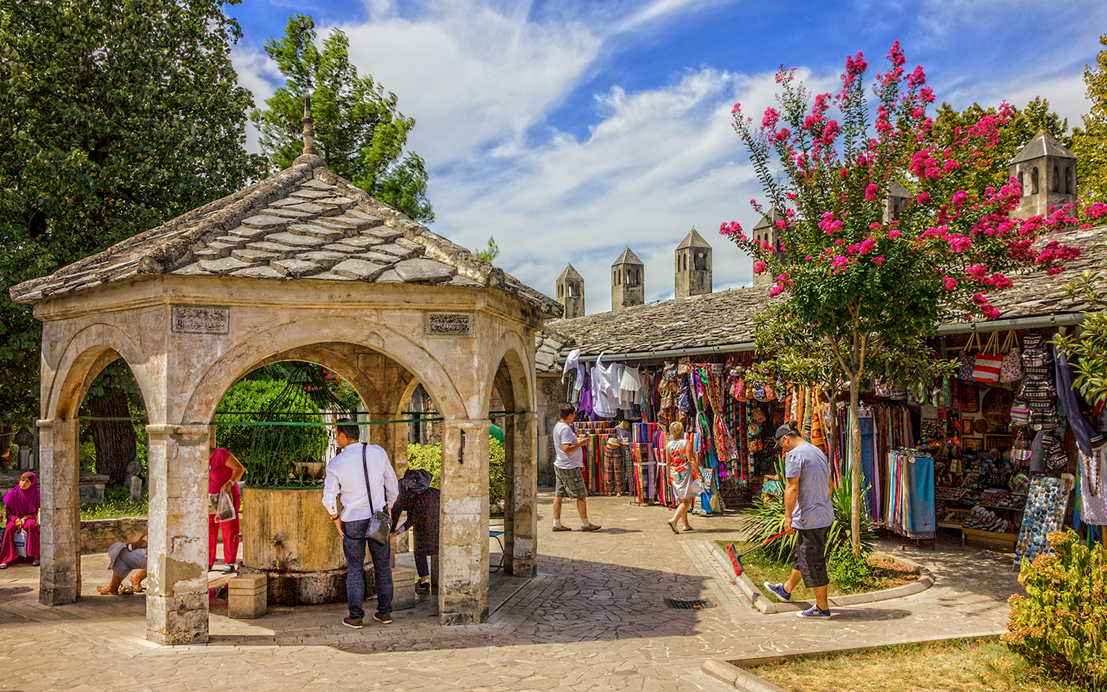 Visitors at a stone pavilion and market stalls in Mostar old town.