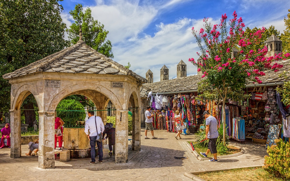 Visitors at a stone pavilion and market stalls in Mostar old town.