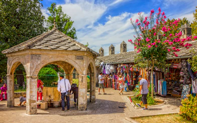 Visitors at a stone pavilion and market stalls in Mostar old town.