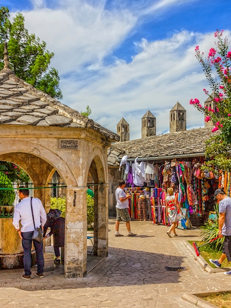Visitors at a stone pavilion and market stalls in Mostar old town.