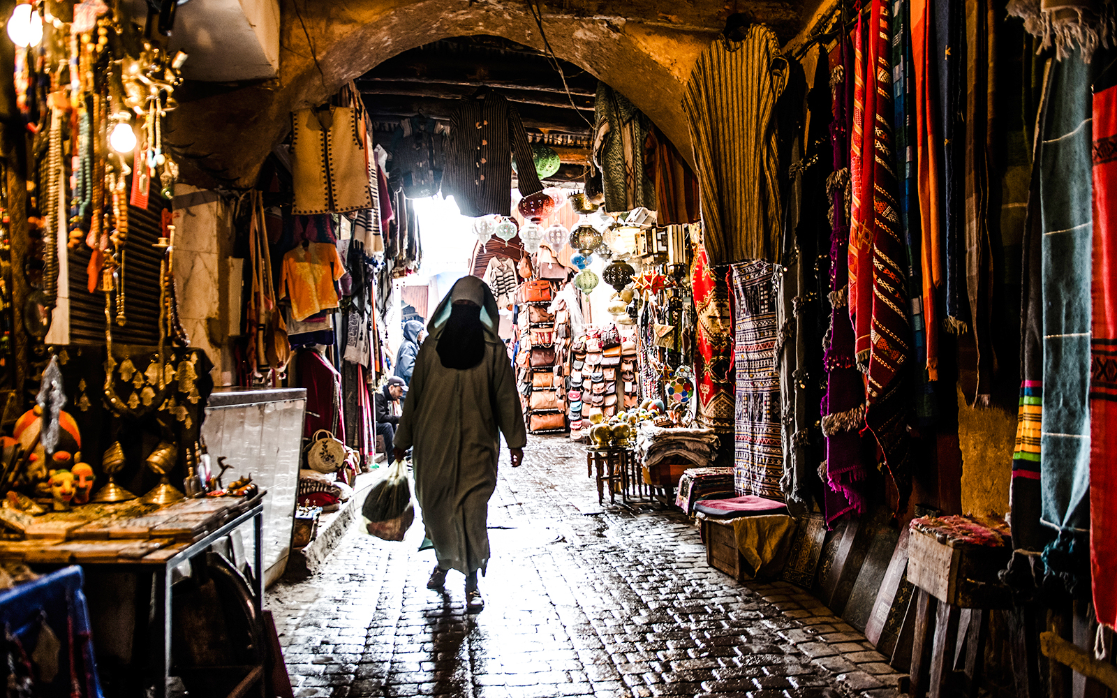 Marrakech market alley with colorful textiles and lanterns during night walking tour.