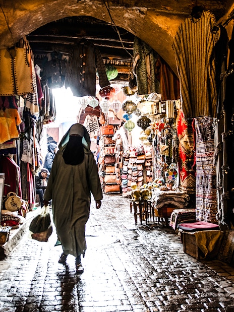 Marrakech market alley with colorful textiles and lanterns during night walking tour.