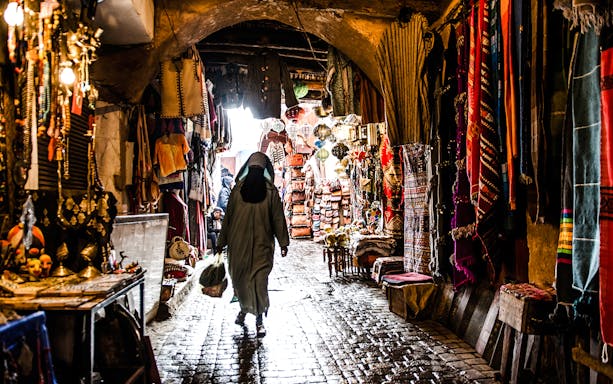 Marrakech market alley with colorful textiles and lanterns during night walking tour.