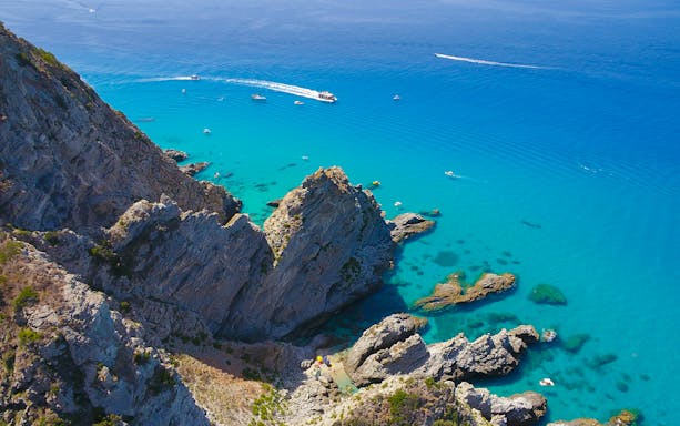 Boat cruising near rocky cliffs and turquoise waters of Capo Vaticano, Tropea.
