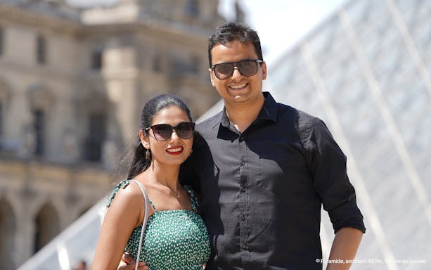 Couple posing in front of the Louvre Pyramid during a professional photoshoot in Paris.