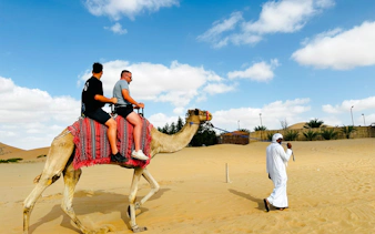 Camel ride during sunrise desert safari in Abu Dhabi with guide leading through sand dunes.