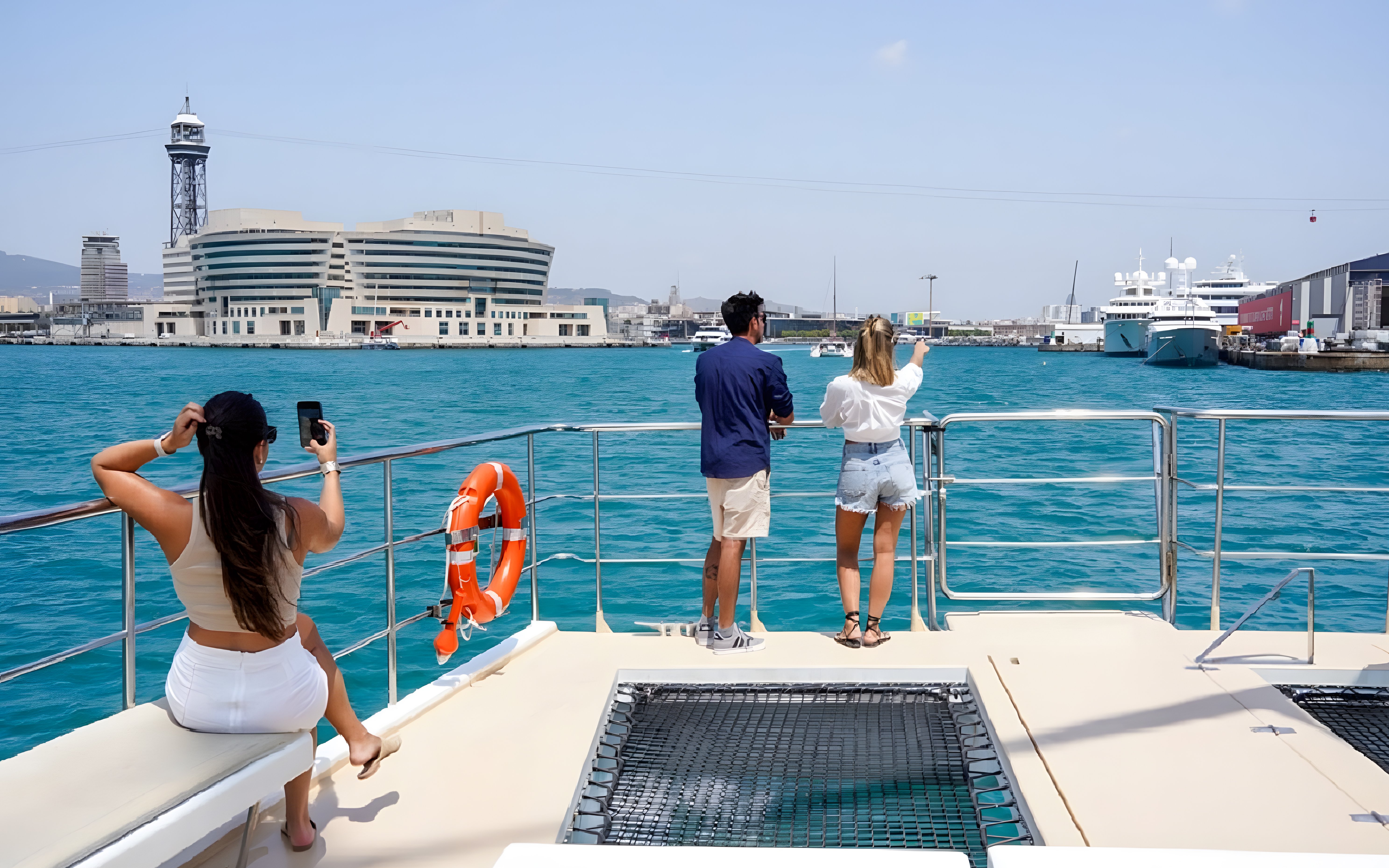 Tourists on Eco Catamaran Cruise in Barcelona harbor, viewing cityscape and yachts.