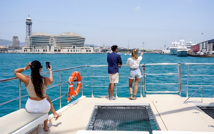 Tourists on Eco Catamaran Cruise in Barcelona harbor, viewing cityscape and yachts.