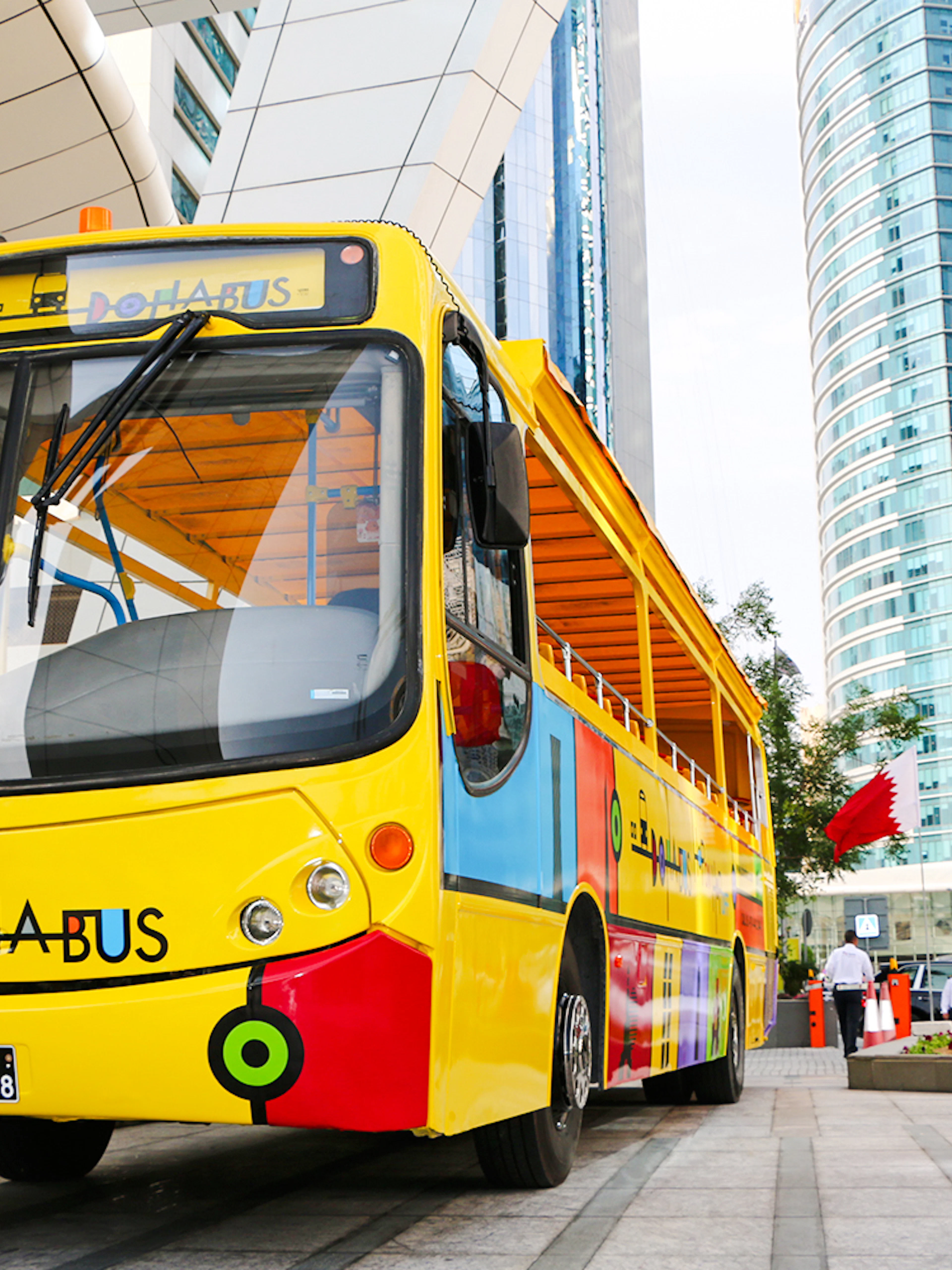 Colorful Doha tour bus in front of modern skyscrapers with Qatar flags.