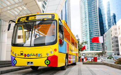 Colorful Doha tour bus in front of modern skyscrapers with Qatar flags.