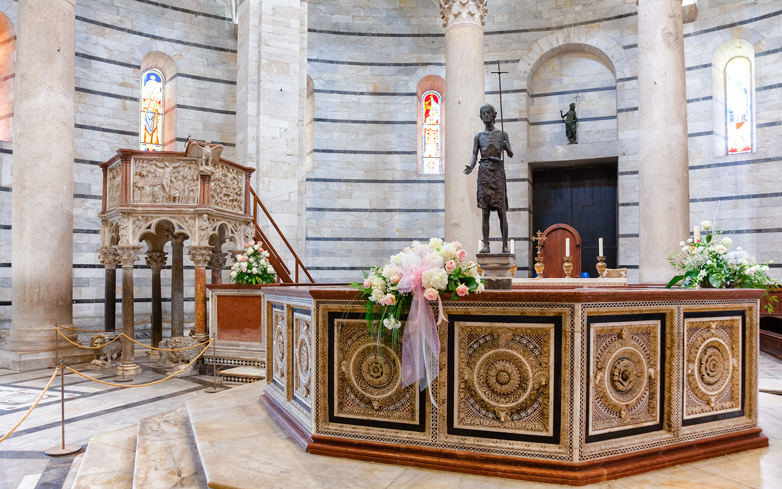 Baptistery of Pisa interior with ornate pulpit and floral decorations.