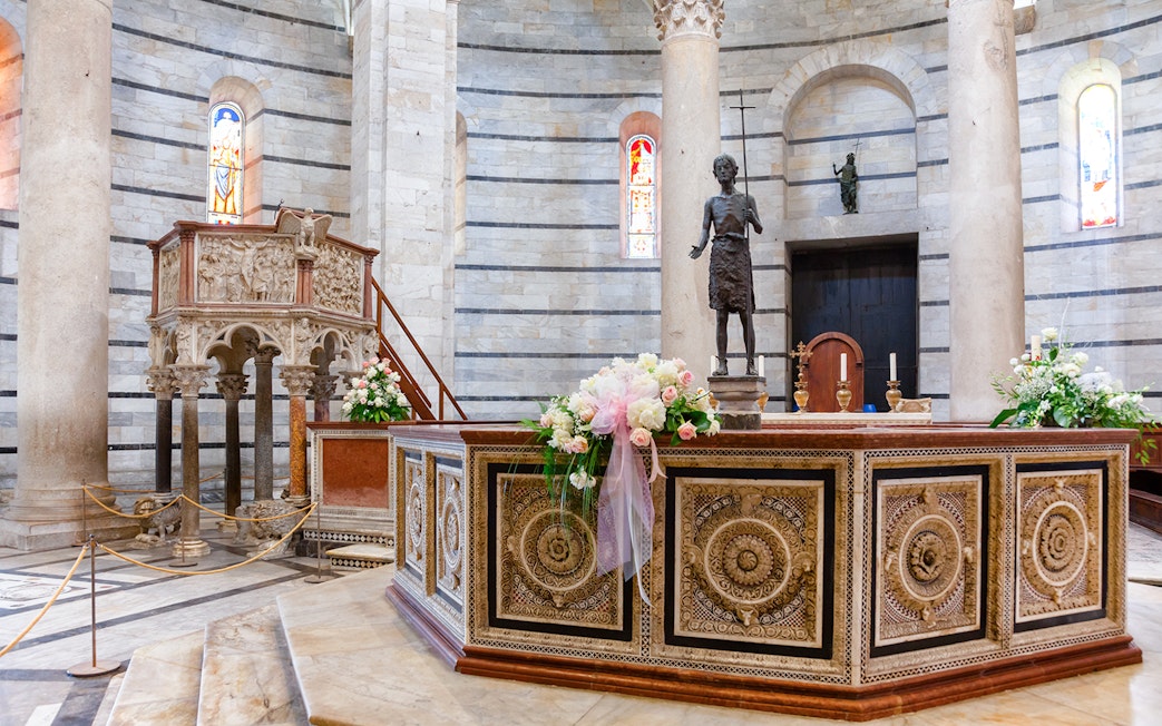 Baptistery of Pisa interior with ornate pulpit and floral decorations.