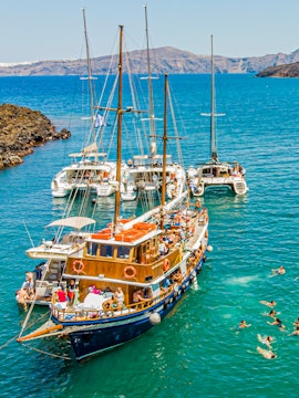 Boats anchored near Santorini hot springs with people swimming in the Aegean Sea.