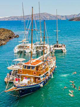 Boats anchored near Santorini hot springs with people swimming in the Aegean Sea.