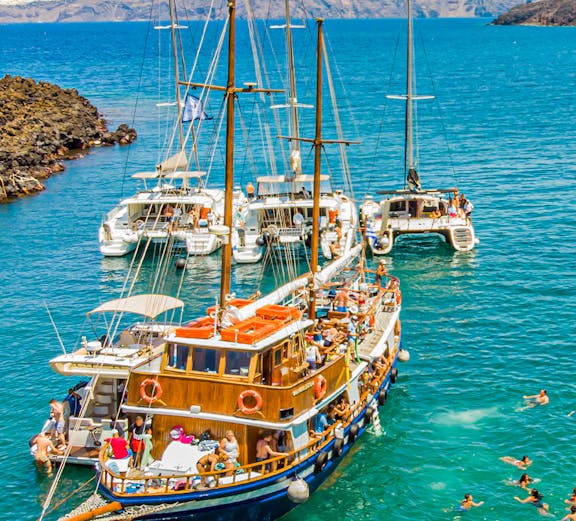 Boats anchored near Santorini hot springs with people swimming in the Aegean Sea.