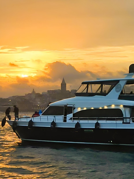 Yacht cruising on the Bosphorus at sunset with Istanbul skyline in the background.