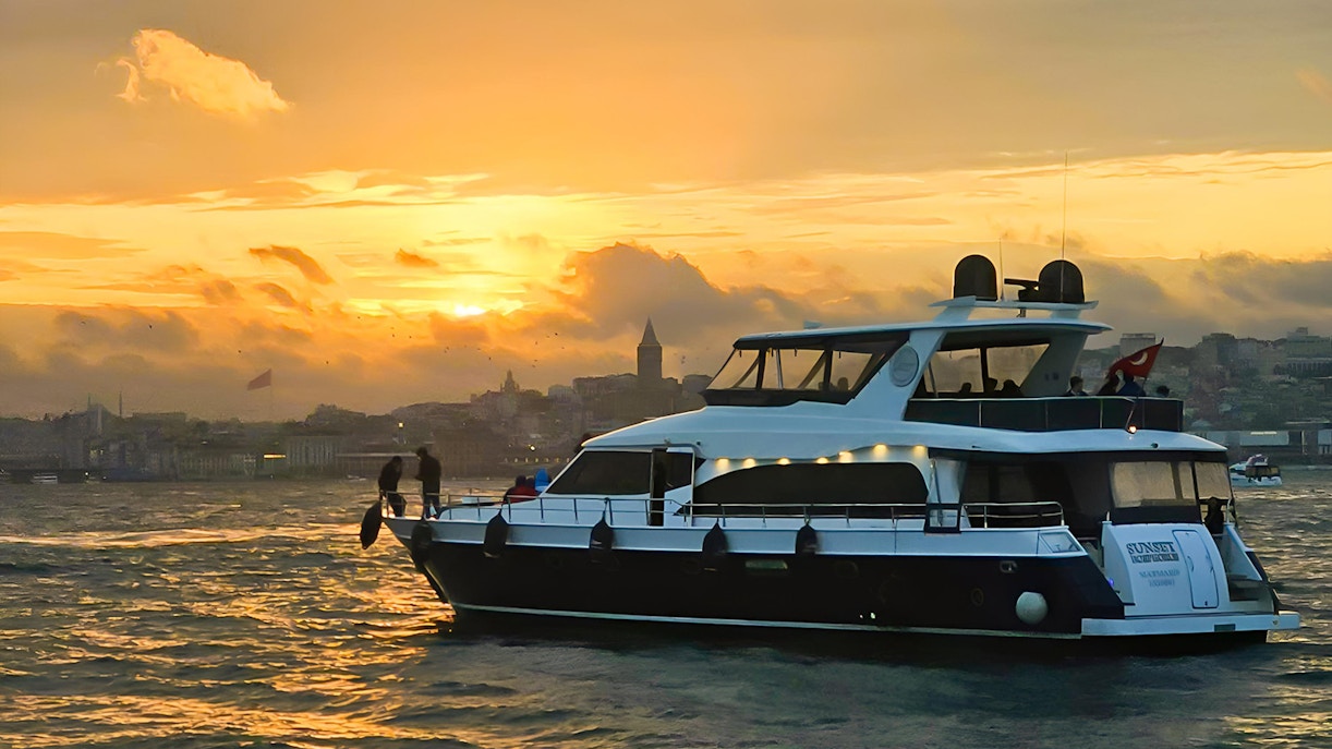 Yacht cruising on the Bosphorus at sunset with Istanbul skyline in the background.