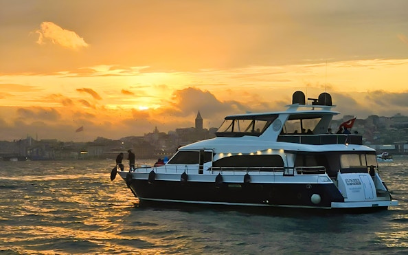Yacht cruising on the Bosphorus at sunset with Istanbul skyline in the background.