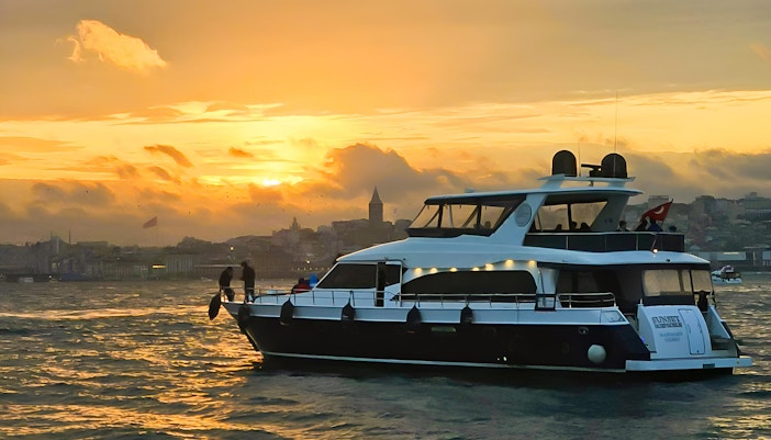 Yacht cruising on the Bosphorus at sunset with Istanbul skyline in the background.