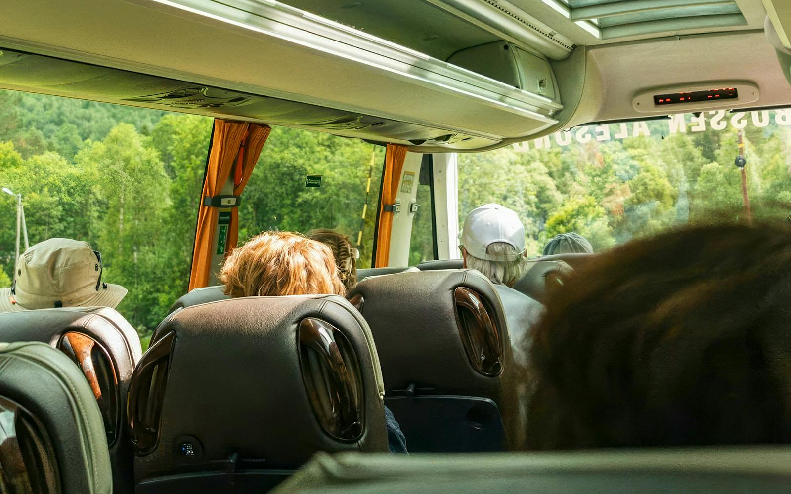 Bus interior with passengers on Ålesund-Geiranger-Ålesund Fjord tour, scenic forest view outside.