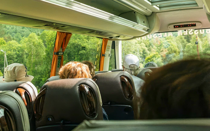Bus interior with passengers on Ålesund-Geiranger-Ålesund Fjord tour, scenic forest view outside.