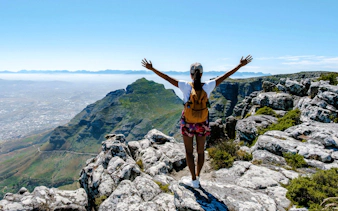 Person with arms raised on Table Mountain overlooking Cape Town's landscape.