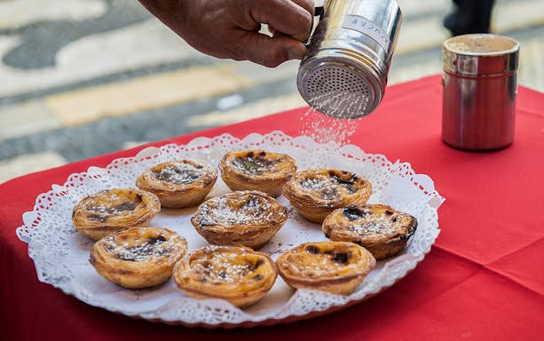 Pastéis de nata being sprinkled with sugar on a Lisbon walking tour.