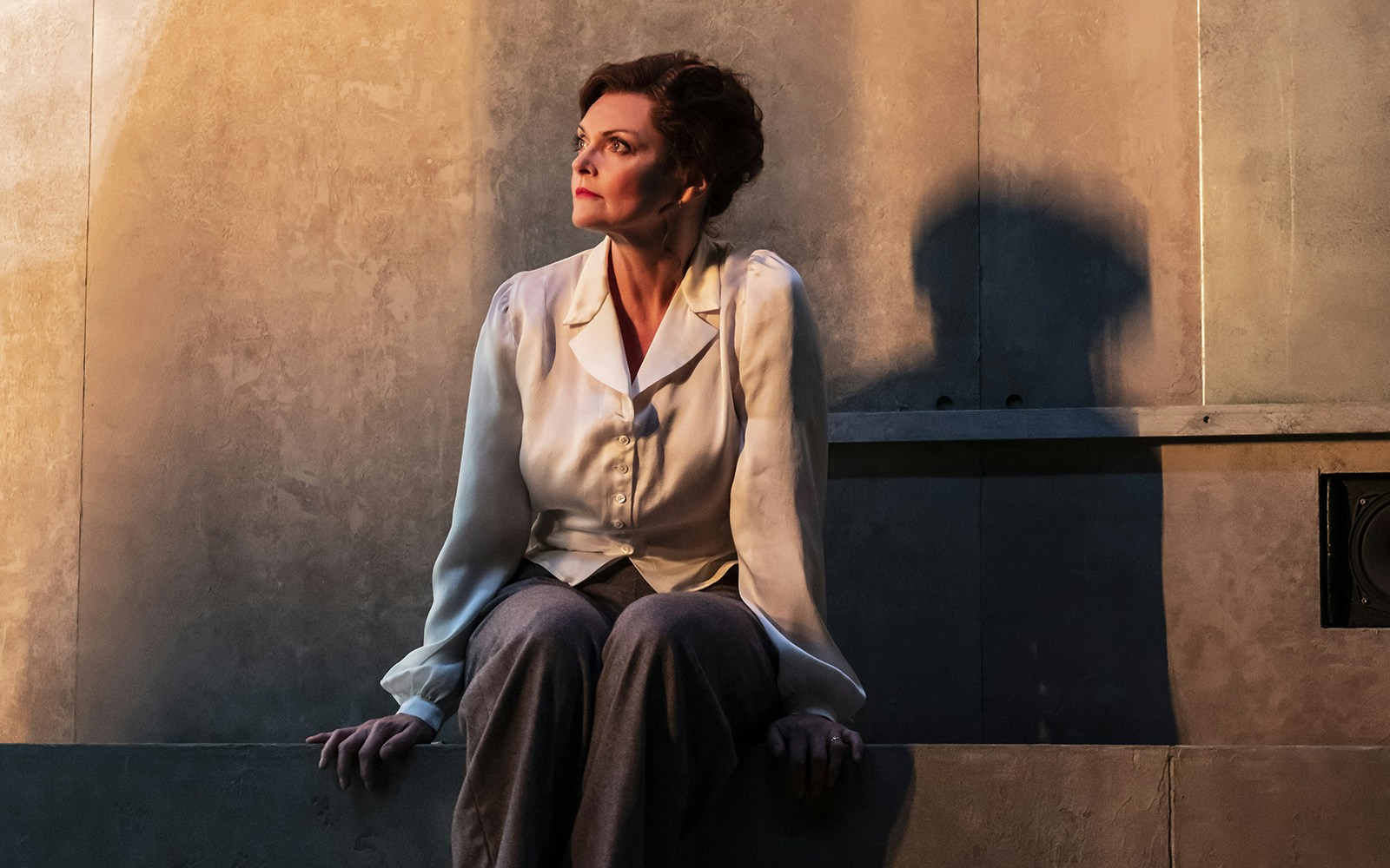 A person sitting against a textured wall, looking contemplative.