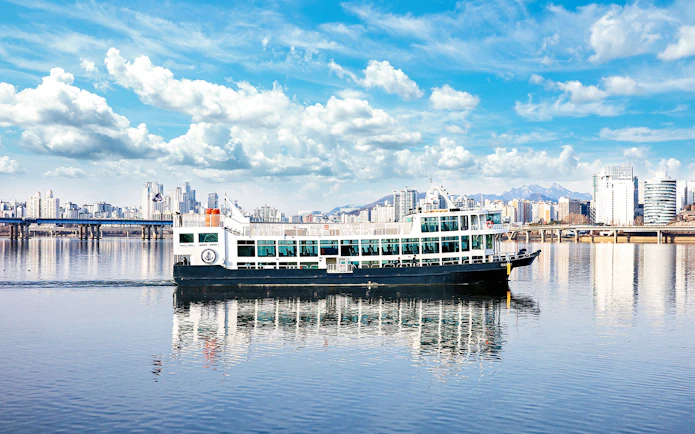 Eland Cruise ship on Hangang River with Seoul skyline in the background.